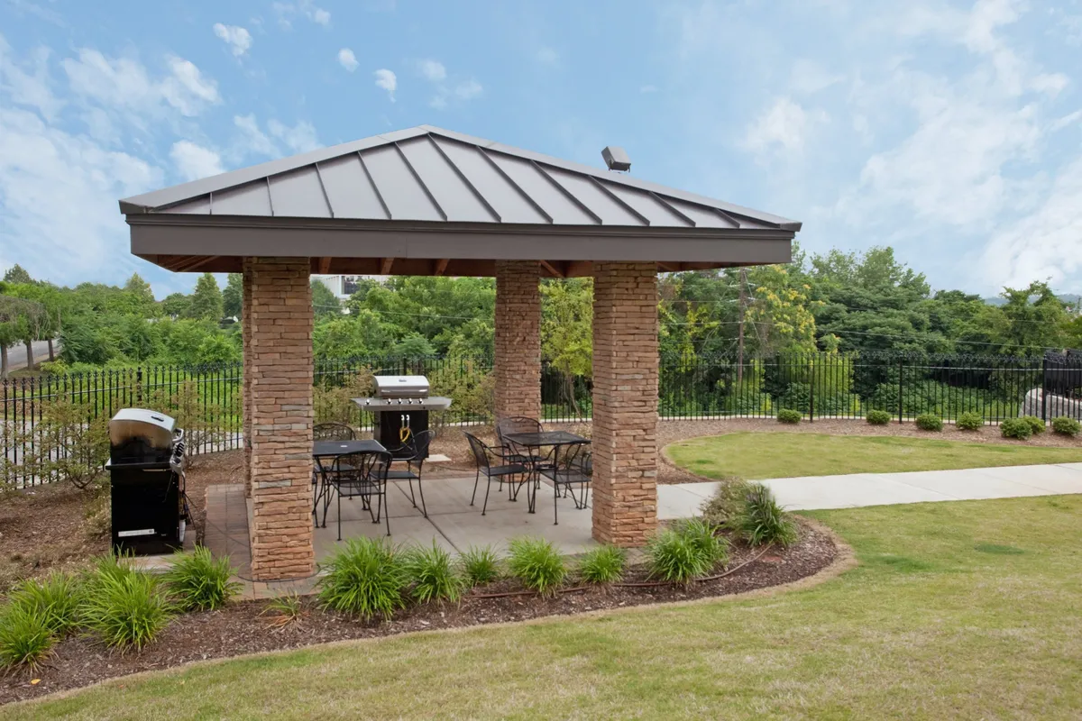 An outdoor pavilion area is depicted with a grill, comfortable seating, and appealing landscaping—an ideal space for social gatherings, outdoor dining, or relaxing after a day out. The scene is casual and inviting, blending the comfort of home with the excitement of urban exploration.