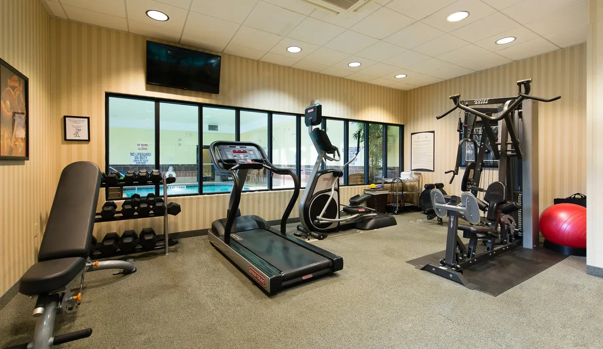 The hotel’s fitness center is shown with a variety of modern exercise equipment, including treadmills, an elliptical machine, a weight bench, and an exercise ball. The space is designed for both solo and group workouts, promoting an active, healthy lifestyle.