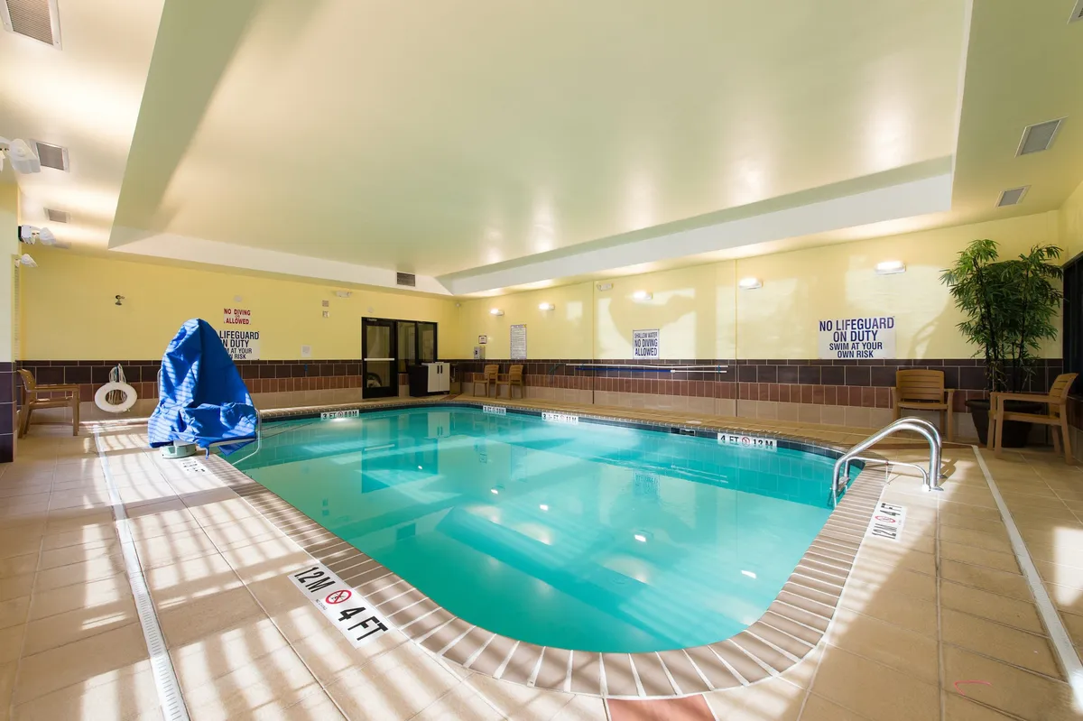 A bright indoor swimming pool area, featuring a blue cover on a poolside chair, poolside seating for relaxation, and lush tropical plants that add a refreshing, inviting atmosphere. The space encourages both recreation and unwinding after a day of activity.