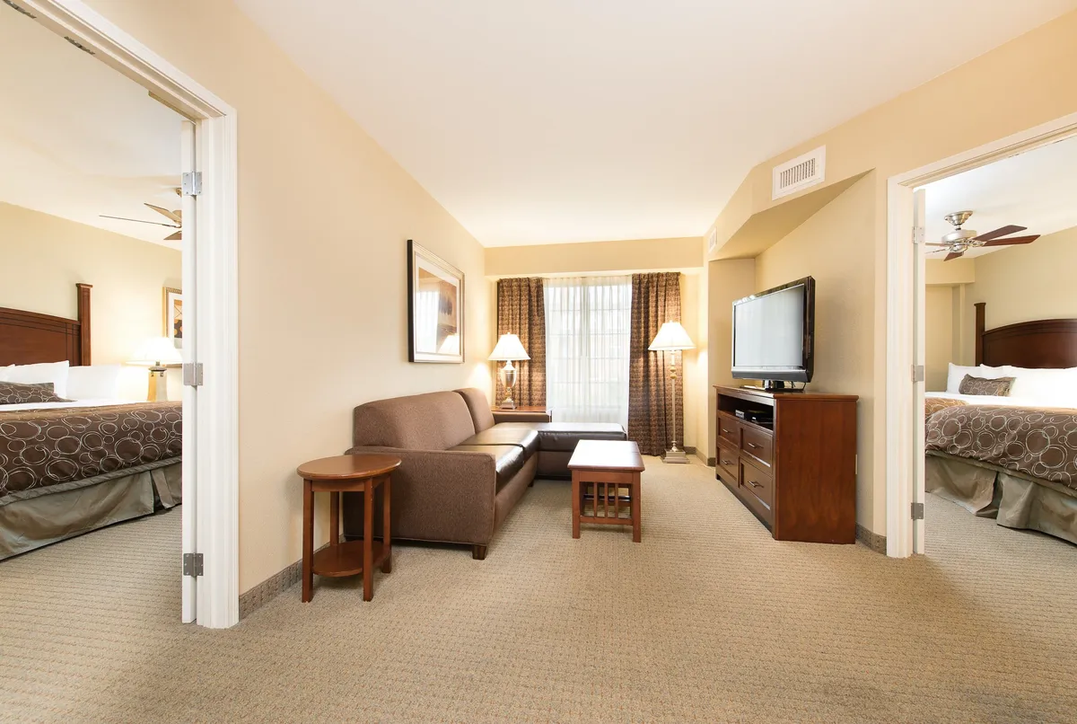 The image showcases a warmly furnished living room with a plush sofa, a modern coffee table, and a large TV, all bathed in natural light from a window with soft curtains. The inviting setup suggests a perfect space for relaxing, socializing, or unwinding after a day exploring downtown Columbia.