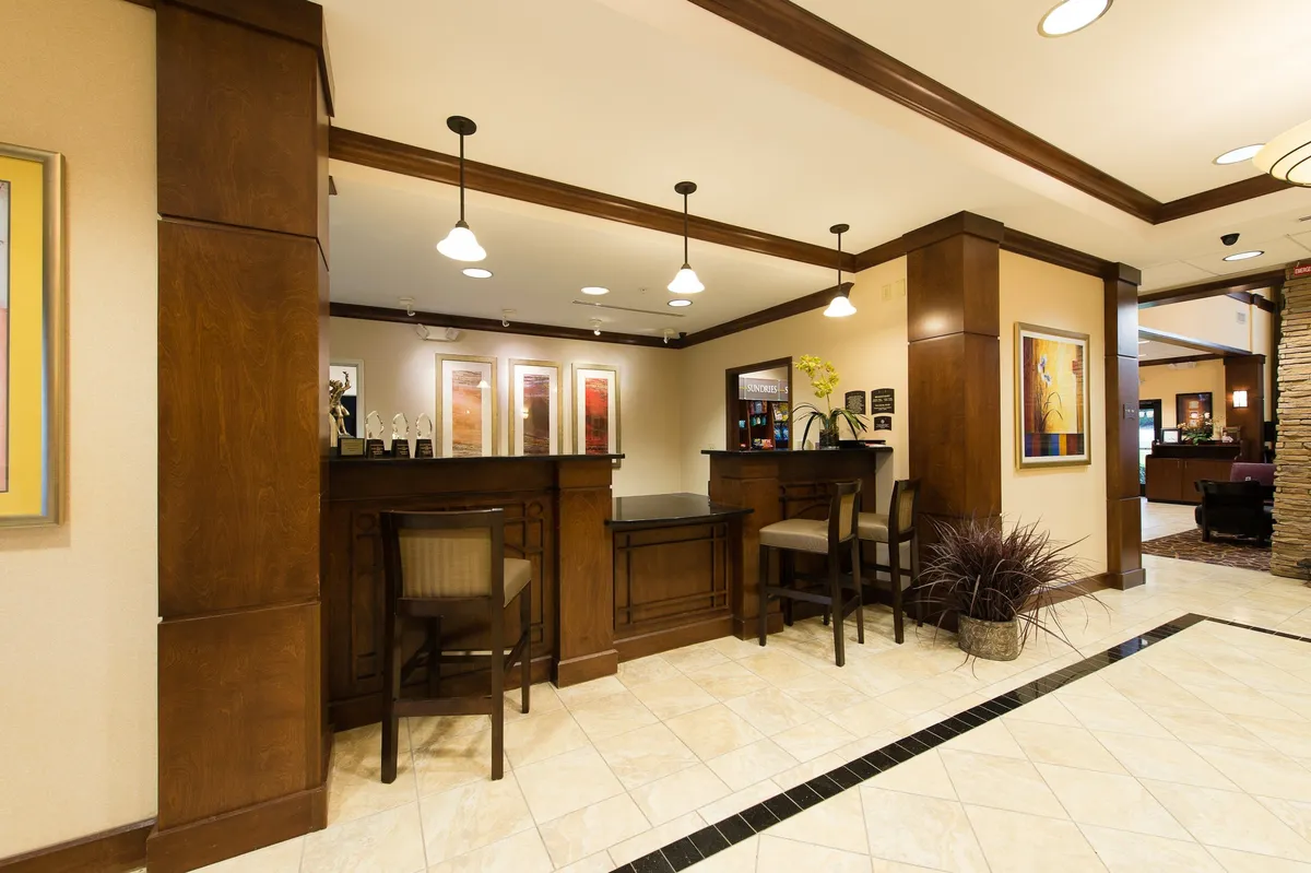 The image depicts the Staybridge Suites Columbia's inviting reception area, featuring a welcoming reception desk, comfortable seating arrangements, and tasteful artwork on the walls. Guests are being checked in, while others relax or socialize, setting a friendly and professional atmosphere.
