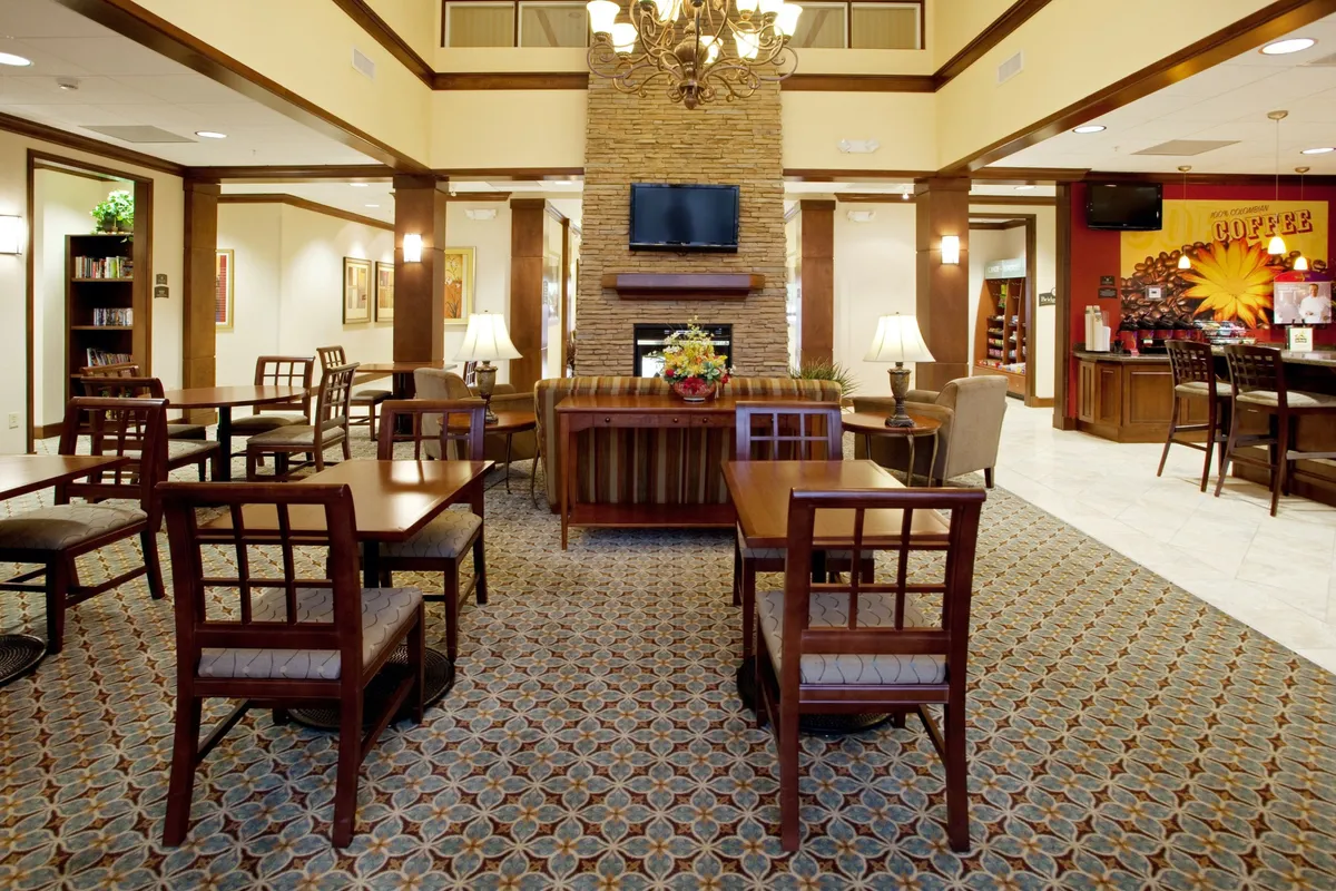 A central seating area anchored by a fireplace, with a coffee bar and decorative wall art. The mood is communal and inviting, offering a comfortable space for reading, socializing, or simply relaxing with a beverage.