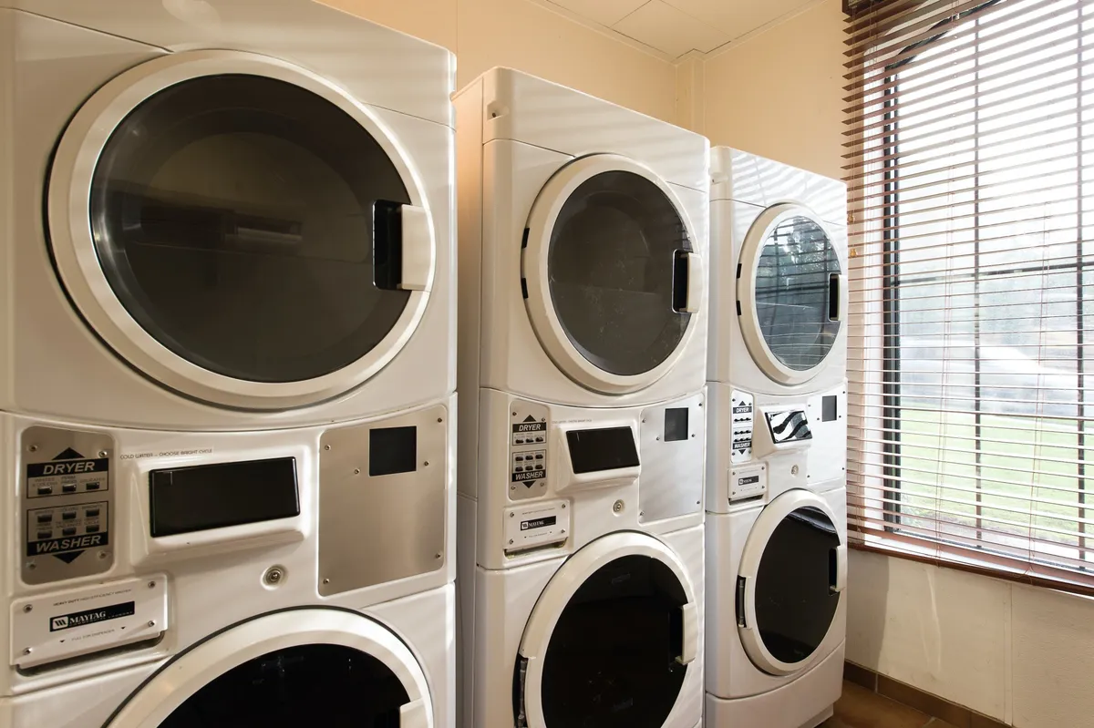 A practical and efficient laundry area featuring stacked washers and dryers beneath a window with blinds. The space is tidy and convenient, reflecting on-site laundry facilities that are especially useful for longer stays.