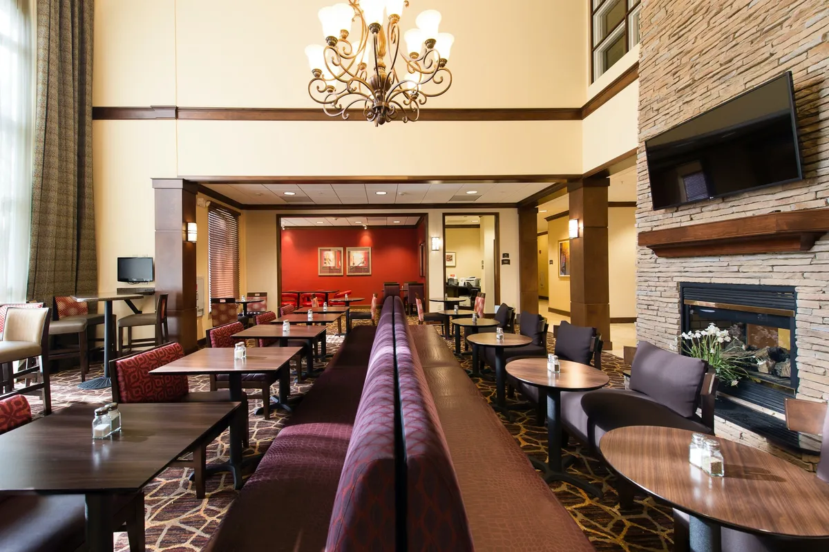 A spacious, inviting living area with a stone fireplace, chandelier, comfortable seating, and wall art. The scene is arranged for relaxation, socializing, or working, with cozy corners and a laptop-friendly atmosphere.